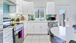 Una cocina moderna con armarios blancos, una estufa de acero inoxidable y un comedor con mesa y sillas.