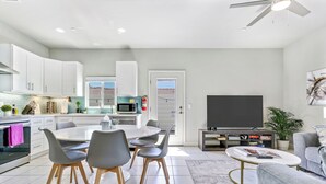 Una cocina moderna con armarios blancos, una mesa de comedor con sillas, un televisor de pantalla plana y un ventilador de techo.