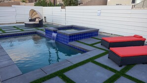 Un patio trasero con piscina, jacuzzi y dos sillas de descanso.