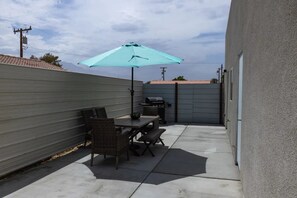 Une terrasse avec une table et des chaises, un barbecue et un parasol bleu.