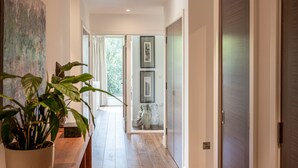 Um corredor com piso de madeira, um vaso com planta e uma porta que dá para outro quarto.