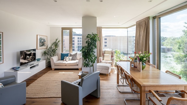 Uma sala de estar moderna com sofá, televisão, mesa de jantar e uma janela grande com vista para prédios.