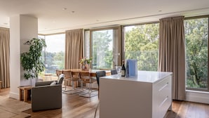 Uma sala de estar moderna com piso de madeira, uma área de jantar com mesa e cadeiras, uma janela grande com cortinas e uma planta em vaso.