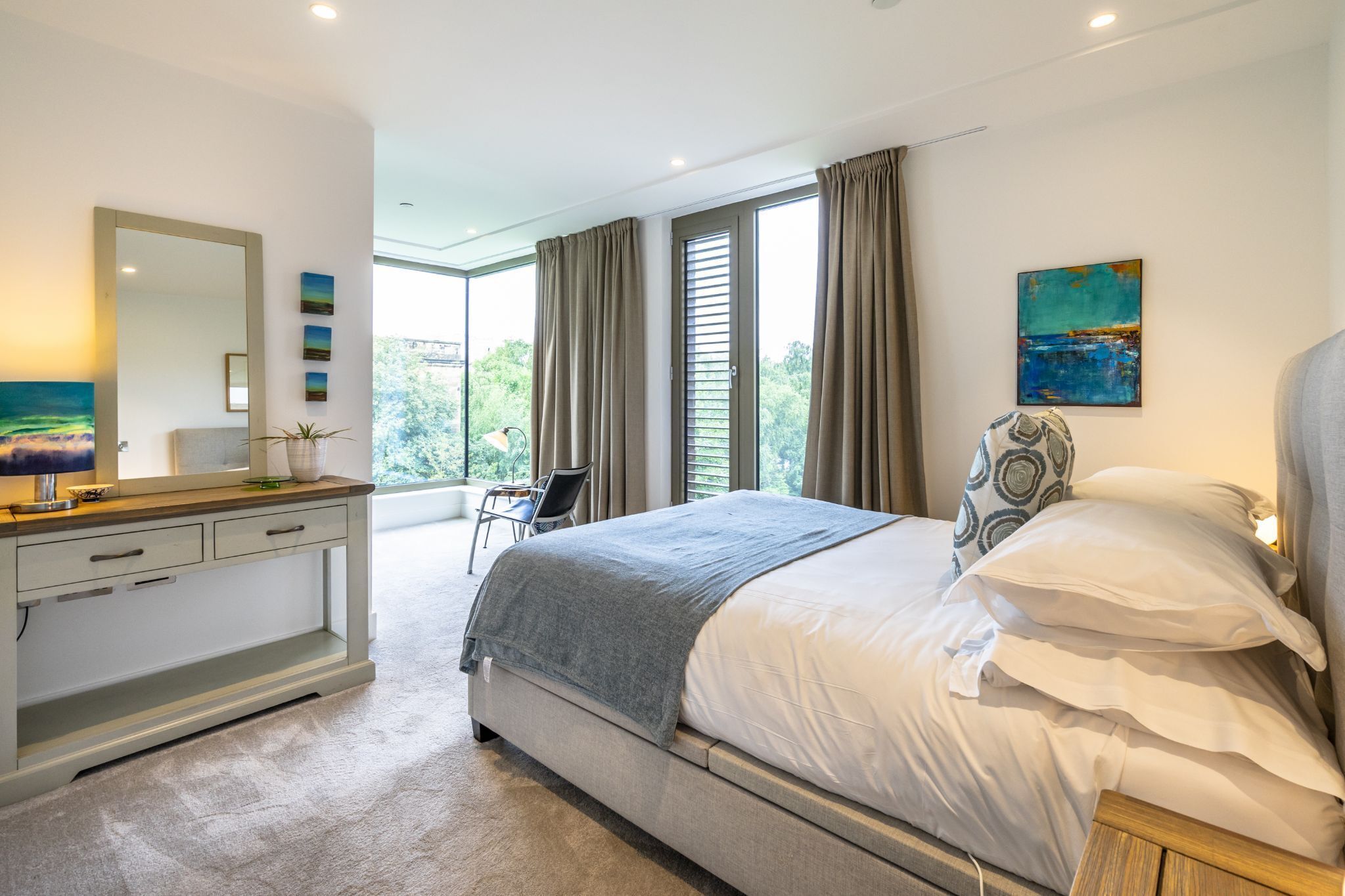 A modern bedroom with a large bed, a bedside table, a dresser, and a window with curtains.