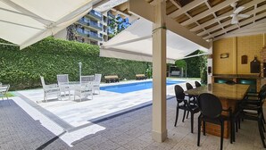 A poolside area with a barbecue and outdoor seating. - Casa Amarela - Riviera (Bertioga)