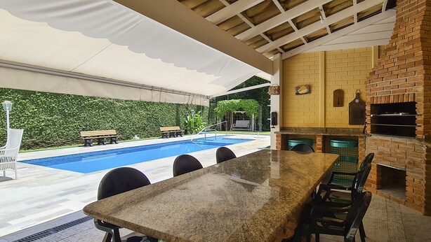 An outdoor kitchen with a brick oven, a pool, and a covered patio area. - Casa Amarela - Riviera (Bertioga)