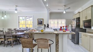 A spacious kitchen with a dining area, featuring a granite countertop, stainless steel appliances, and a ceiling fan. - Casa Amarela - Riviera (Bertioga)