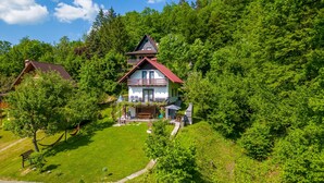 A two-story house with a red roof and a balcony, surrounded by lush greenery and trees. - Ideal oasis for a vacation surrounded with forest (Kupa, Brod na Kupi)