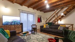 A cozy living room with a wooden ceiling, a black sofa with yellow and gray cushions, a wooden coffee table, and a television on the left. - Ideal oasis for a vacation surrounded with forest (Kupa, Brod na Kupi)
