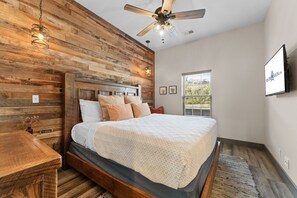 A bedroom with a wooden headboard, a bed with multiple pillows, a ceiling fan, and a window with blinds. - Private Putting Green Retreat with Firepit, Hot Tub, Free Tickets, Views & Community Indoor Pool (Branson)