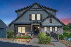 A two-story house with a stone facade, a front porch with chairs, and a stone staircase leading to the entrance. - Private Putting Green Retreat with Firepit, Hot Tub, Free Tickets, Views & Community Indoor Pool (Branson)