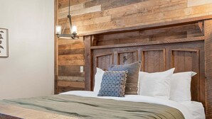 Een bed met houten hoofdbord, nachtkastje en hanglamp.