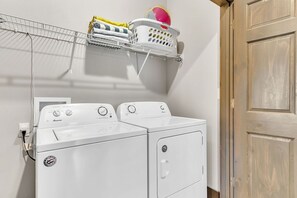 A laundry area with two front-loading washing machines, a drying rack with clothes and a beach ball, and a wooden door. - Private Putting Green Retreat with Firepit, Hot Tub, Free Tickets, Views & Community Indoor Pool (Branson)