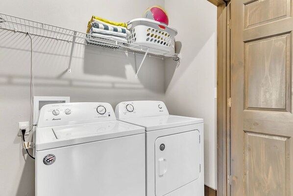 A laundry area with two front-loading washing machines, a drying rack with clothes and a beach ball, and a wooden door.