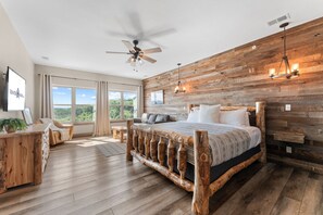 A bedroom with a wooden bed frame, a ceiling fan, a large window with curtains, and a view of the outdoors. - Private Putting Green Retreat with Firepit, Hot Tub, Free Tickets, Views & Community Indoor Pool (Branson)