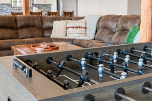 A foosball table in a living room with a brown leather couch and a coffee table.