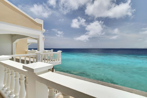 A balcony with white railings overlooking turquoise ocean waters.
