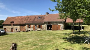 A stone farmhouse with a sloped roof, a large open garage, and a grassy yard. - Beautiful luxury restored gîte with private solar heated pool. (St. Paul la Roche)