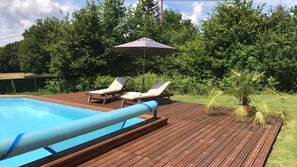Un pontile in legno con piscina, due poltrone relax e una palma.