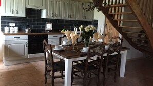 A dining area with a wooden table set for four, surrounded by dark wooden chairs. A chandelier hangs above, and a staircase with wooden railings is visible to the right. - Beautiful luxury restored gîte with private solar heated pool. (St. Paul la Roche)