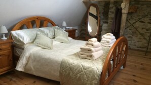 A wooden bed with a quilted bedspread, a wooden nightstand with a lamp, a mirror, and a stack of towels on the bed. - Beautiful luxury restored gîte with private solar heated pool. (St. Paul la Roche)