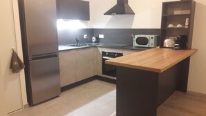 A compact kitchen with a refrigerator, stove, microwave, and a wooden island. - Appartement salon cuisine chambre jardin. Sécurisé. Neuf. hygiène +++ (la Roche sur Foron)