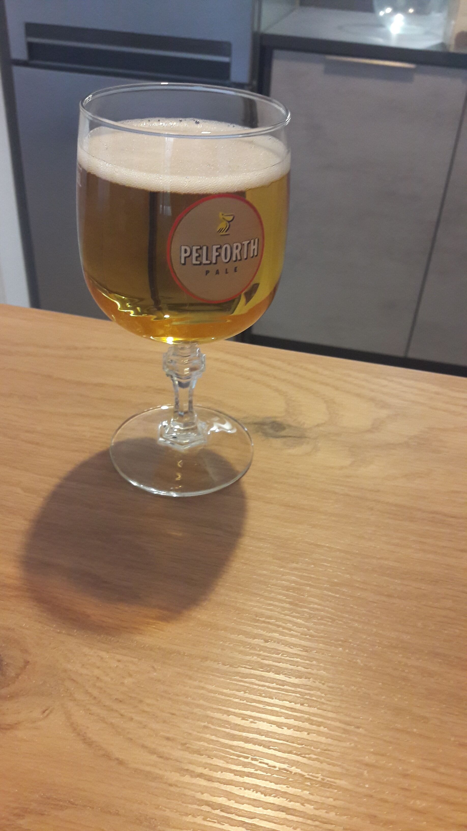 A glass of Pelforth Pale beer on a wooden table.