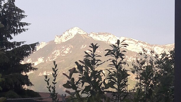 A view of a mountain range with snow-capped peaks, a fence, and some greenery in the foreground. - Appartement salon cuisine chambre jardin. Sécurisé. Neuf. hygiène +++ (la Roche sur Foron)