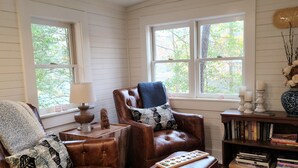 A cozy living room with a brown leather sofa, a matching ottoman, and a wooden bookshelf.