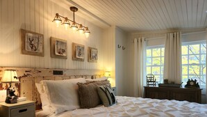 A bedroom with a large bed, a nightstand with a lamp, and wall-mounted artwork.