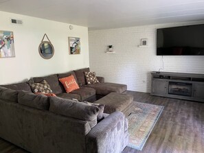 A living room with a sectional sofa, a flat-screen TV, a fireplace, and a patterned rug. - Lovely 1 bed room apartment, all to yourself. (Merrillville)