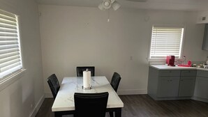 Ein Essbereich mit Tisch und Stühlen, einem Deckenventilator und einer Küchenzeile mit Schränken und Arbeitsfläche.