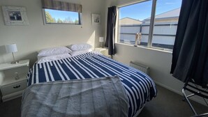 Ein Hotelzimmer mit einem großen Bett, einem Fenster mit Vorhängen, einem Nachttisch mit Lampe und einem Heizkörper.