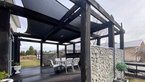 Eine Terrasse im Freien mit Holzdeck, Steinmauer und überdachtem Sitzbereich mit Stühlen und Tischen.