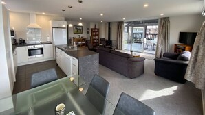 Eine moderne Wohnung mit Küche, Essbereich und Wohnzimmer. Sie umfasst einen Esstisch mit Stühlen, eine Couch und einen Fernseher.