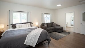 Quarto com uma cama grande, um sofá e um banheiro visível por uma porta aberta.
