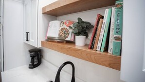 Uma cozinha com cafeteira, uma planta e uma estante com livros de receitas.