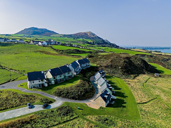 A modern hotel with a long, curved building, situated in a lush, green valley with a mountain in the background.