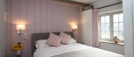 A bedroom with a bed, two wall-mounted lamps, a window with curtains, and a vase on the windowsill.