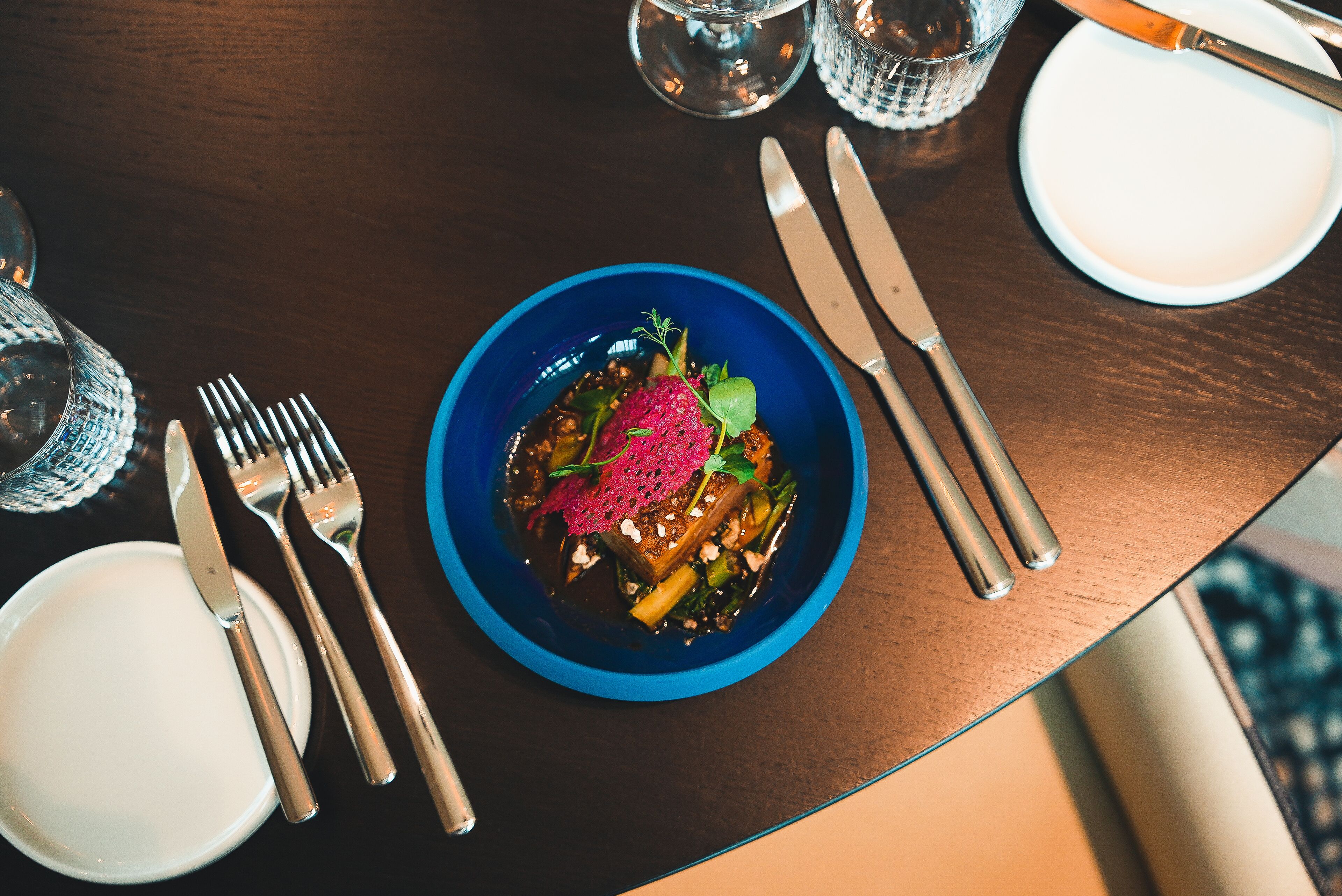 A dining table with a blue bowl of food, silverware, and a white plate.