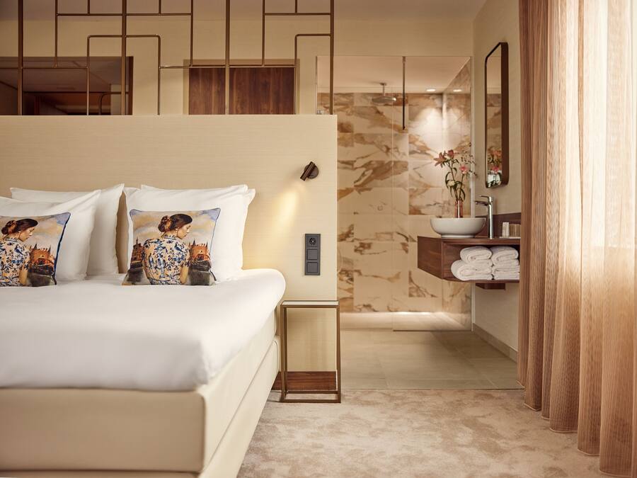 A modern hotel room with a large bed, a bathroom with a marble wall, and a wooden vanity.