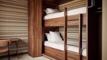Una cama litera con estructura de madera y ropa de cama blanca, una pequeña mesa con una silla, y una pared con diseño.