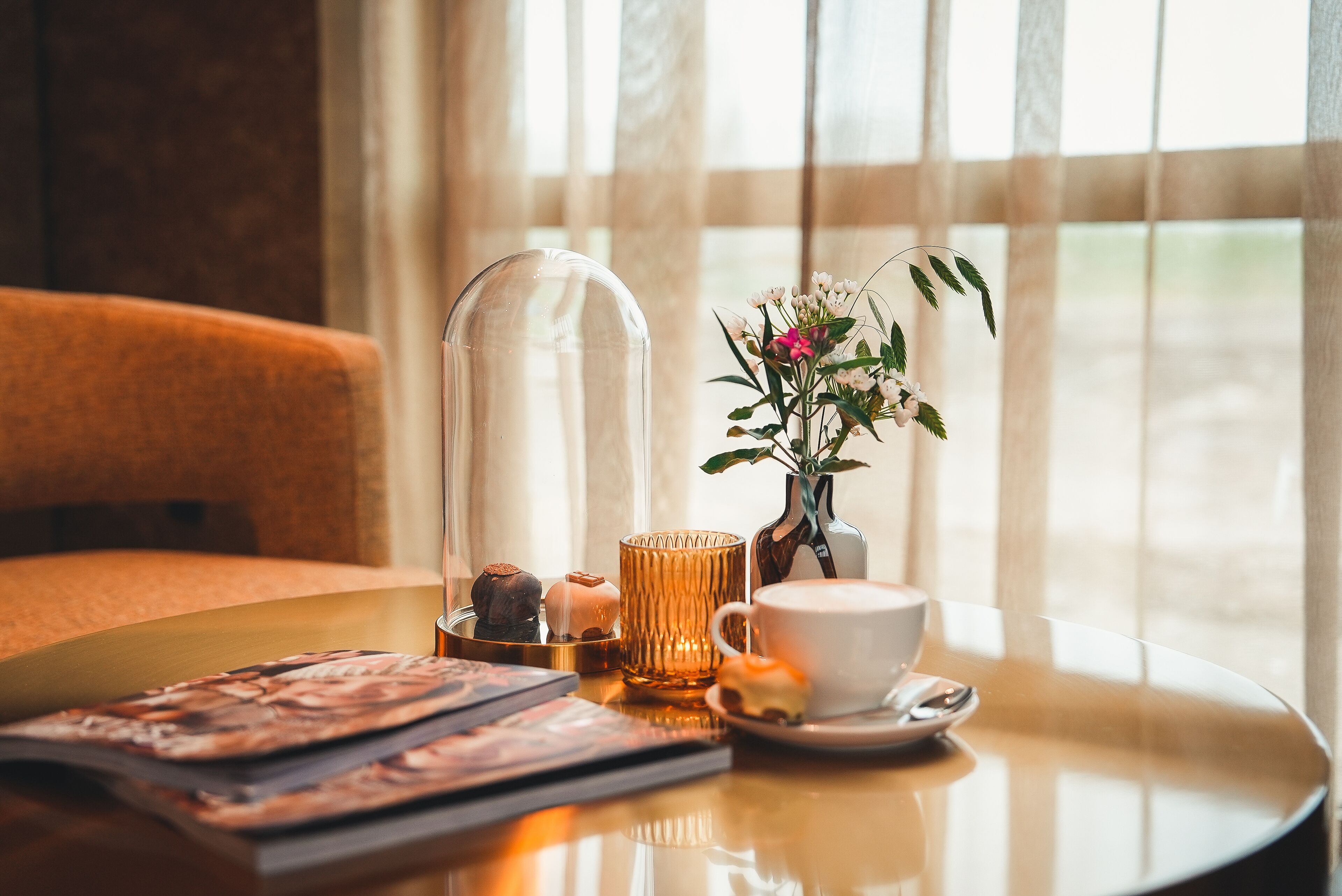 A table with a cup, saucer, a glass container, a vase with flowers, and a book.