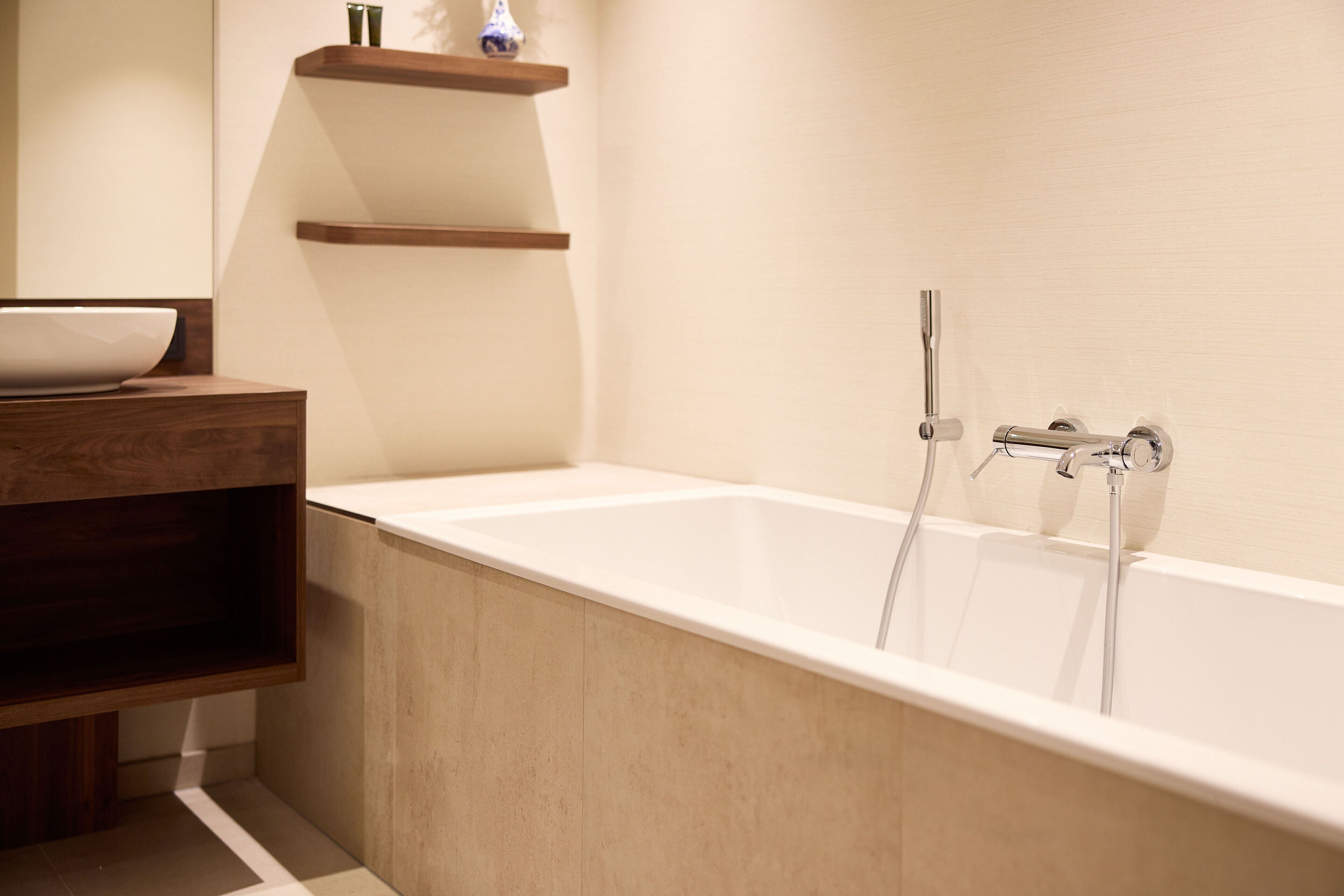 A modern bathroom with a freestanding bathtub, wooden shelves, and a white basin.
