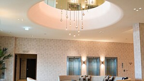 A spacious lobby with a modern design, featuring a central seating area, a reception desk, and a visible elevator.