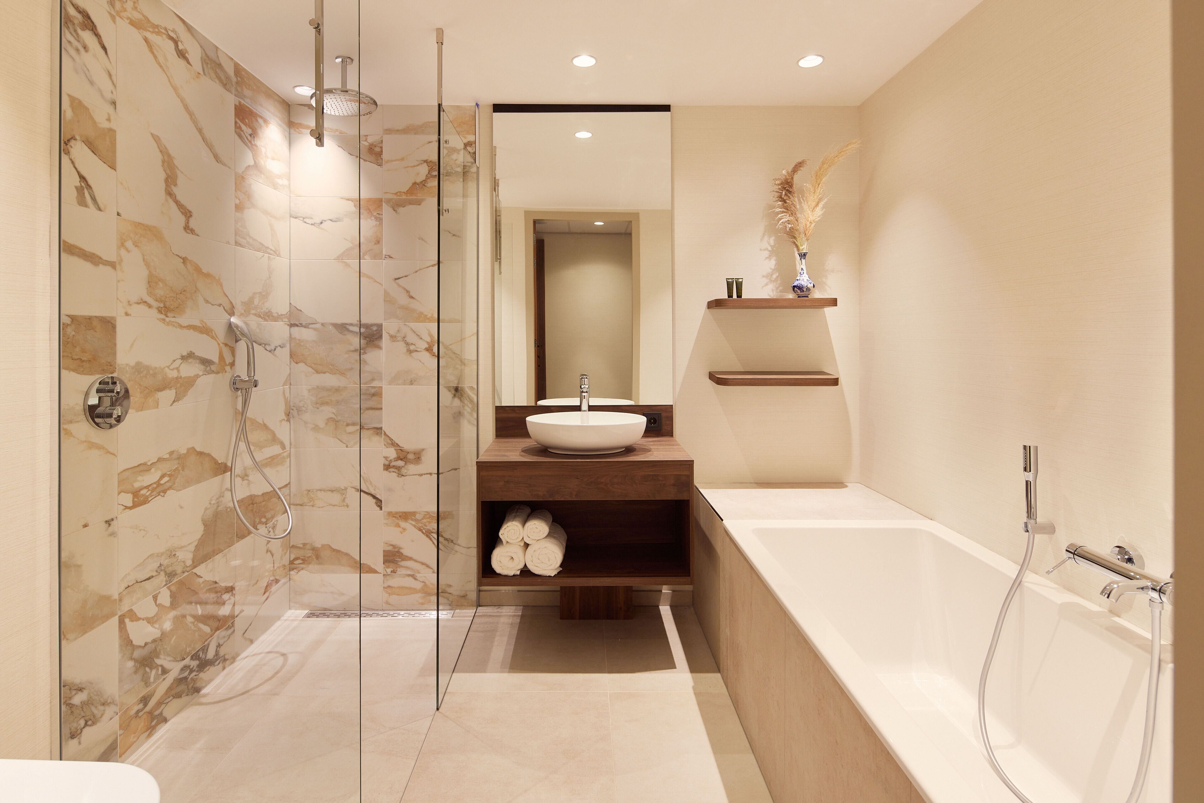A modern bathroom with a glass-enclosed shower, a large bathtub, and a marble-tiled wall.