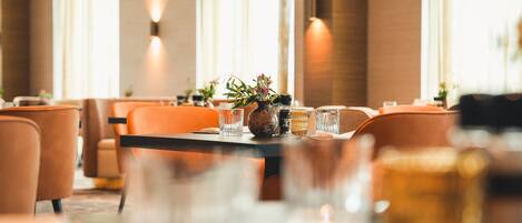 A dining area with orange chairs, a table with a vase and glasses, and wall-mounted lights.