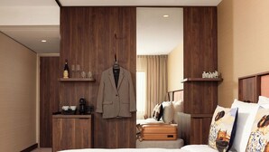 A hotel room with a wooden wardrobe, a bed with white bedding, a suitcase, and decorative pillows.