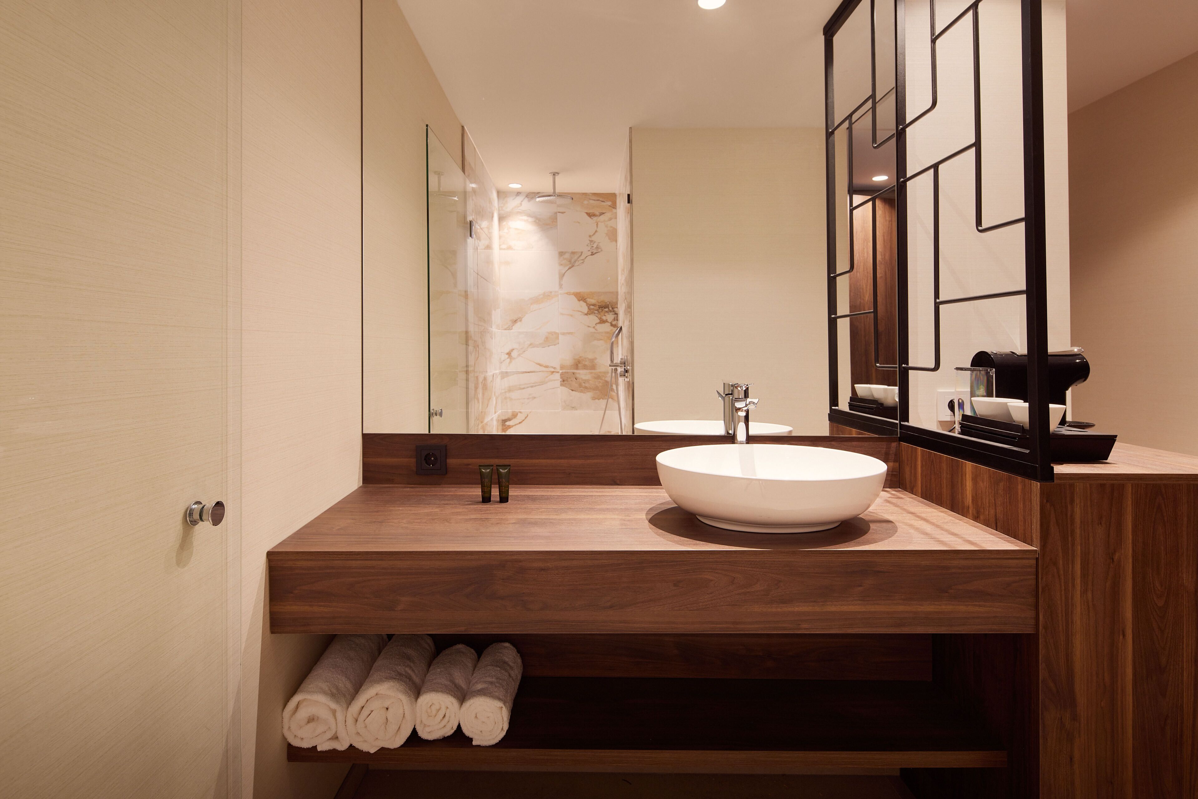 A modern bathroom with a wooden vanity, a large mirror, and a marble shower wall.