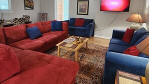 A living room with red and blue sofas, a coffee table, and a TV displaying 'FREE'. - Close to Downtown, Restaurants, Markets , Events ,Beaches and Naval Base! (Pensacola)